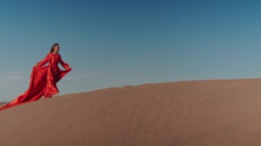 Kum tepelerinde dans eden kırmızı elbiseli Asyalı bir kadın.