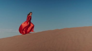 Kum tepelerinde dans eden kırmızı elbiseli Asyalı bir kadın.