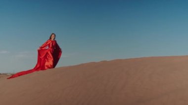 Kum tepelerinde dans eden kırmızı elbiseli Asyalı bir kadın.