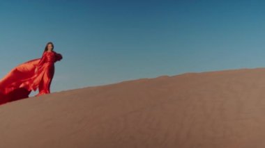 Kum tepelerinde dans eden kırmızı elbiseli Asyalı bir kadın.
