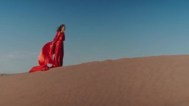 Kum tepelerinde dans eden kırmızı elbiseli Asyalı bir kadın.