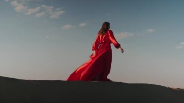 Kum tepelerinde dans eden kırmızı elbiseli Asyalı bir kadın.