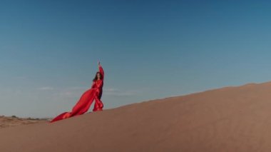 Kum tepelerinde dans eden kırmızı elbiseli Asyalı bir kadın.