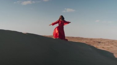 Kum tepelerinde dans eden kırmızı elbiseli Asyalı bir kadın.