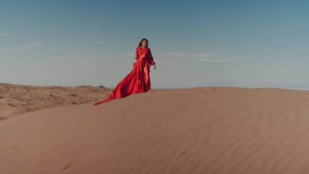 Una donna asiatica in abito rosso che balla sulle dune di sabbia — Video Stock