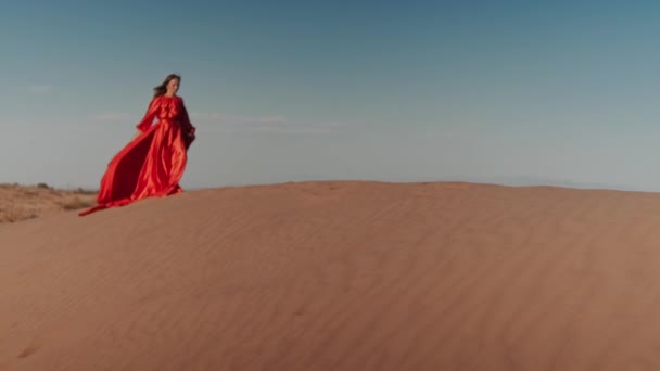 En asiatisk kvinna i röd klänning dansar på sanddyner — Stockvideo