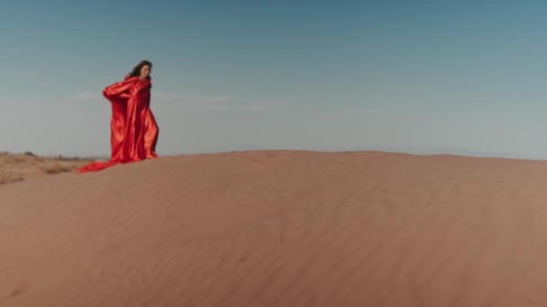 Una mujer asiática en un vestido rojo bailando en dunas de arena — Vídeo de stock