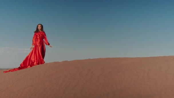 Uma mulher asiática em um vestido vermelho dançando em dunas de areia — Vídeo de Stock