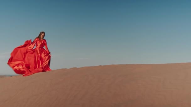 En asiatisk kvinna i röd klänning dansar på sanddyner — Stockvideo