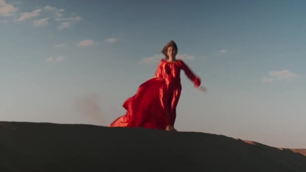 Una donna asiatica in abito rosso che balla sulle dune di sabbia — Video Stock