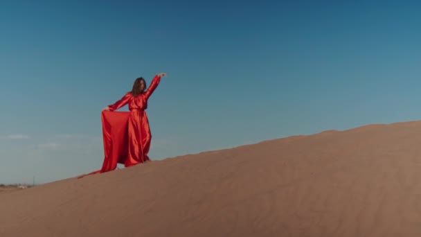 Una mujer asiática en un vestido rojo bailando en dunas de arena — Vídeo de stock