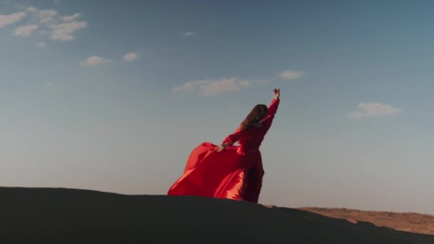 Una mujer asiática en un vestido rojo bailando en dunas de arena — Vídeo de stock