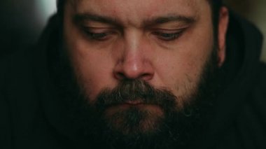 Sakallı bir adam üzgün bir şekilde kameraya bakıyor, statik kamera, yüzüne yakın çekim.