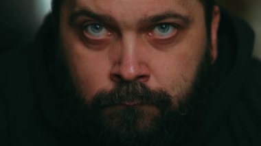 Sakallı bir adam üzgün bir şekilde kameraya bakar ve sakalına dokunur. Sabit kamera, yüzüne yakın plan.