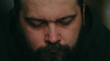 Sakallı bir adam ne yazık ki kameraya bakıyor, statik kamera, yüzüne yakın çekim.