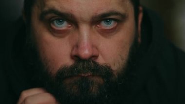 Sakallı bir adam kapüşon takıyor ve üzgün bir şekilde kameraya bakıyor, statik kamera, yüzüne yakın çekim.