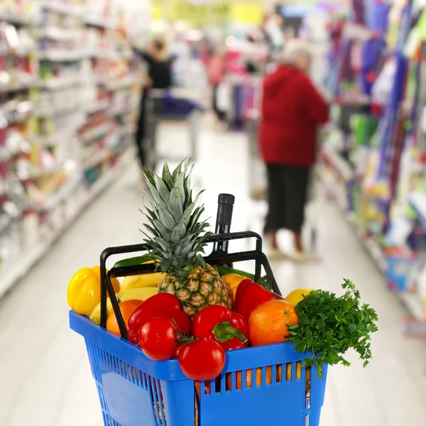 Cesto shopping con generi alimentari sul negozio di sfondo — Foto Stock