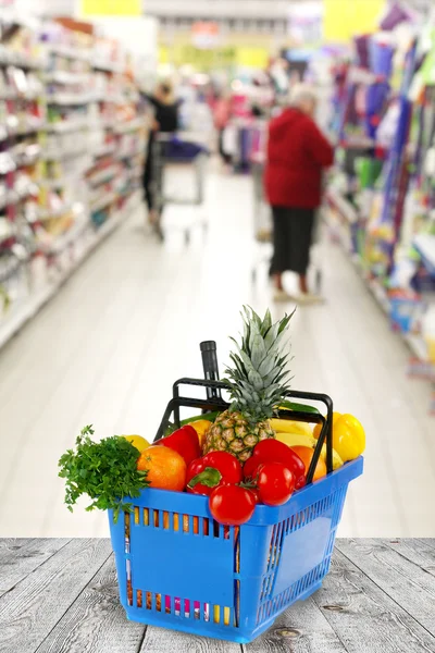 Cesta de compras com mantimentos na loja de fundo — Fotografia de Stock