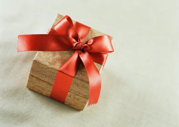 A brown gift with a red satin ribbon and a bow