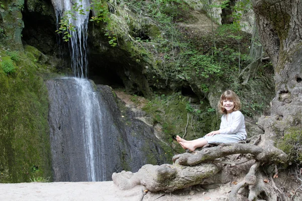 Little girl sitting next to a waterfall — Stock Photo, Image