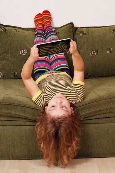 Küçük kız baş aşağı yalan Oda ve tablet ile oynamak — Stok fotoğraf