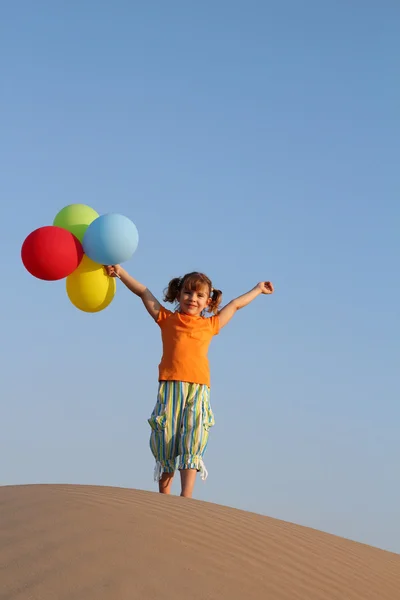 Счастливая маленькая девочка с воздушными шарами, стоящими на песчаной дюне — стоковое фото
