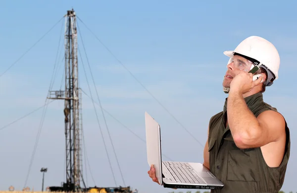 Oil worker with laptop and rig — Stock Photo, Image