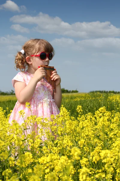 Klein meisje permanent in geel bloem veld en spelen pan pijp — Stockfoto