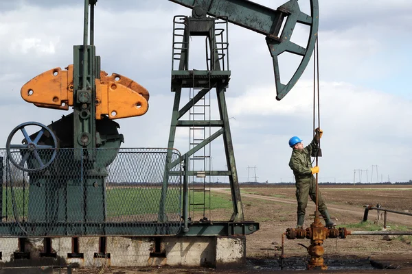 Oil worker standing at pipeline and check pump jack — Stock Photo, Image