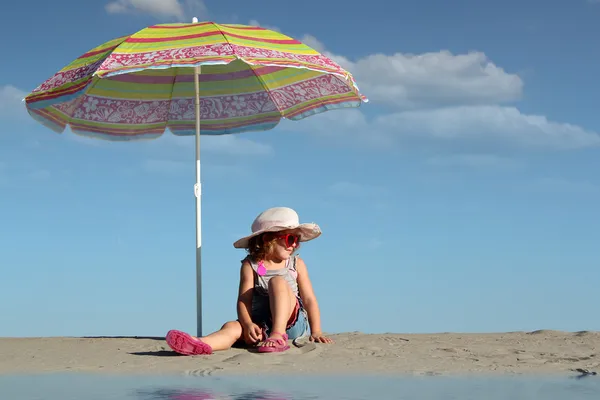 Little girl with sunglasses sitting under sunshade — Stock Photo, Image