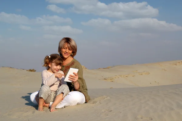 Happy mother and daughter play with tablet pc in desert — Stock Photo, Image