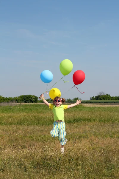 Gelukkig meisje met ballonnen springen op veld — Stockfoto