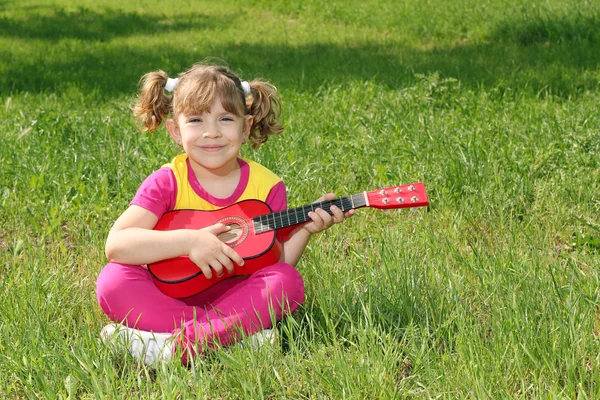 Gelukkig meisje met gitaar zittend op het gras — Stockfoto