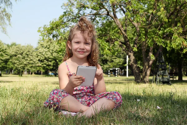 Glückliches kleines Mädchen mit Tablet im Park — Stockfoto