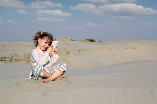 Dziewczynka siedzi na piasku i grać z komputera typu tablet — Zdjęcie stockowe