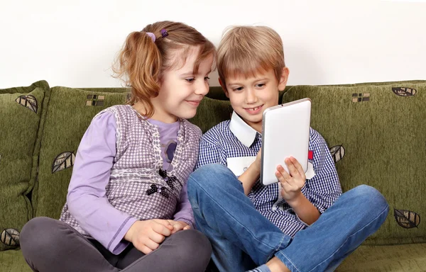 Niña y niño sentado en la cama y jugar con la tableta — Foto de Stock