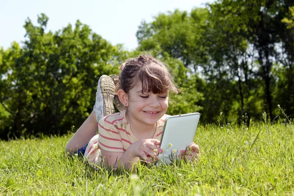 Holčička ležela na trávě a hrát si s počítači tablet pc — Stock fotografie