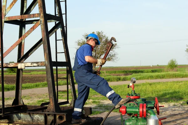 Worker with pipe wrench on oilfield pipeline — Stock Photo, Image