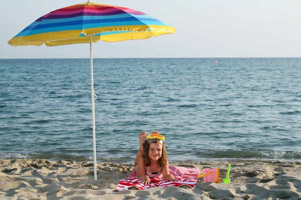 Kleines Mädchen mit Tauchermaske liegt unter Sonnenschirm am Strand — Stockfoto