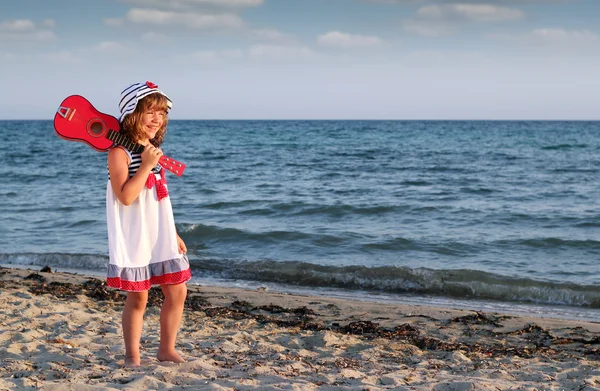 Glückliches kleines Mädchen mit Gitarre am Strand — Stockfoto