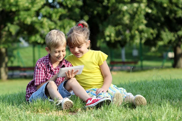 Menino e menina brincam com tablet pc no parque — Fotografia de Stock