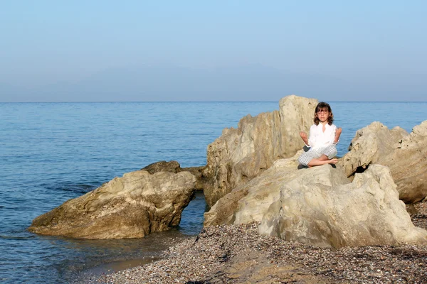 Küçük kız deniz kenarında bir kayanın üzerine oturmuş ve meditasyon — Stok fotoğraf