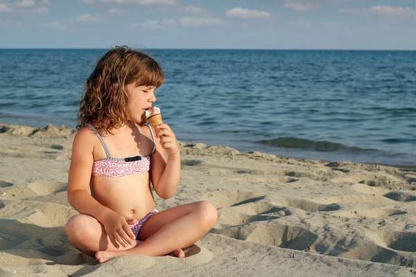 座っている小さな女の子ビーチし、アイスクリームを食べる — ストック写真