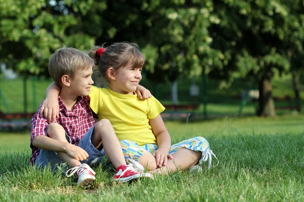 Jongen en meisje, zittend op het gras in park — Stockfoto