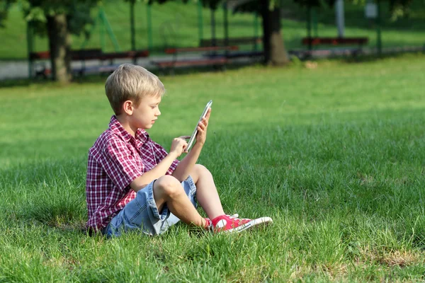 Jongen op gras zitten en spelen met tablet pc — Stockfoto