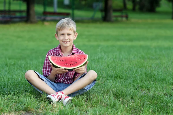 Šťastný chlapec s meloun sedět na trávě — Stock fotografie