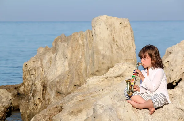 Liten flicka spela saxofon vid havet — Stockfoto