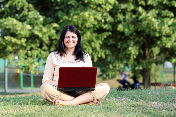 Gelukkig meisje met laptop zitting op gras — Stockfoto