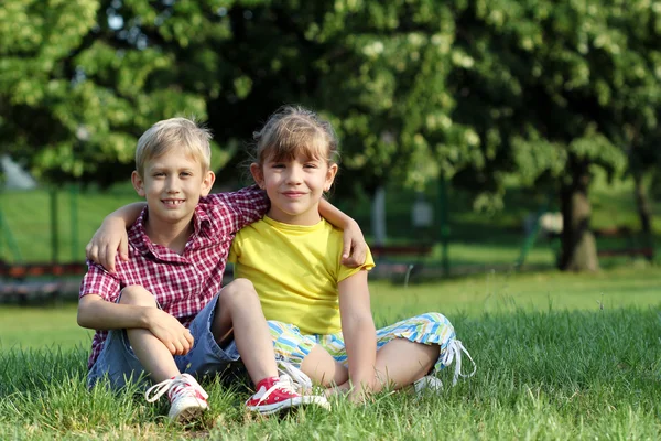 Glückliches kleines Mädchen und Junge auf Gras sitzend — Stockfoto