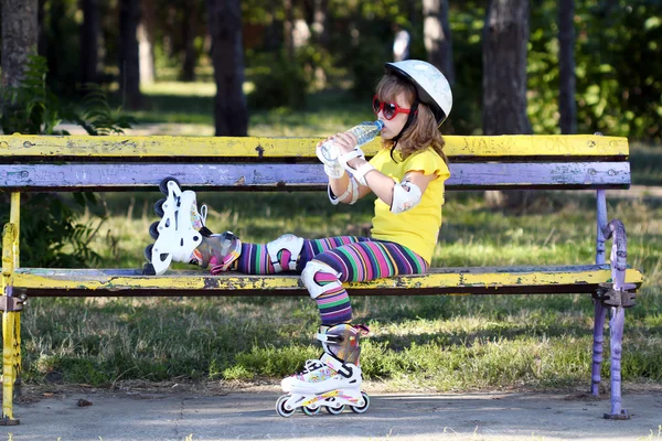 Niña con patines sentada en el banco y beber agua — Foto de Stock